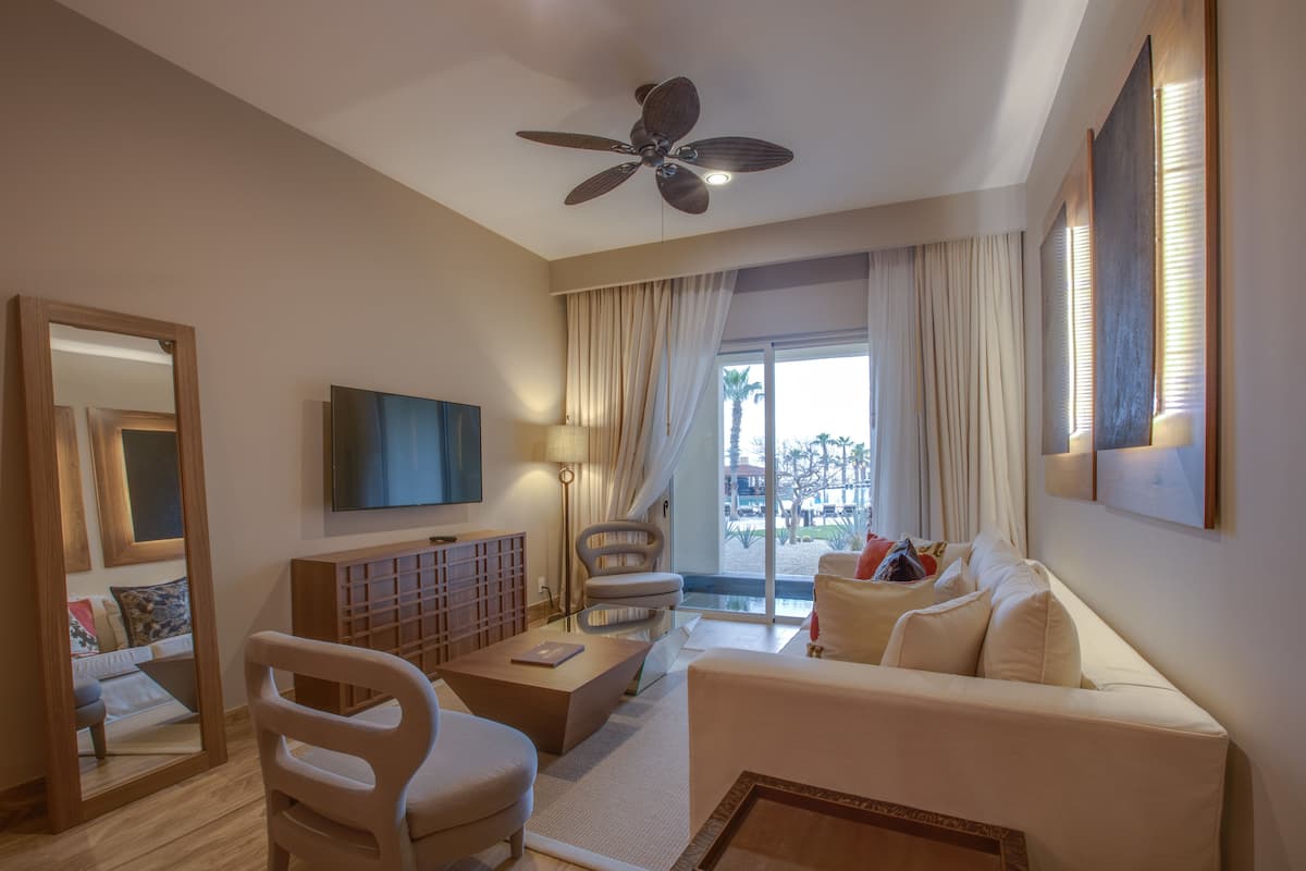 Une chambre d’hôtel moderne équipée d’un ventilateur de plafond, d’un téléviseur à écran plat, d’un canapé, d’une table basse, d’un fauteuil et d’une grande fenêtre avec des rideaux.