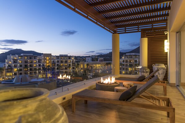 Una terraza en la azotea con sillones de descanso, una chimenea y vistas a un paisaje urbano al anochecer.