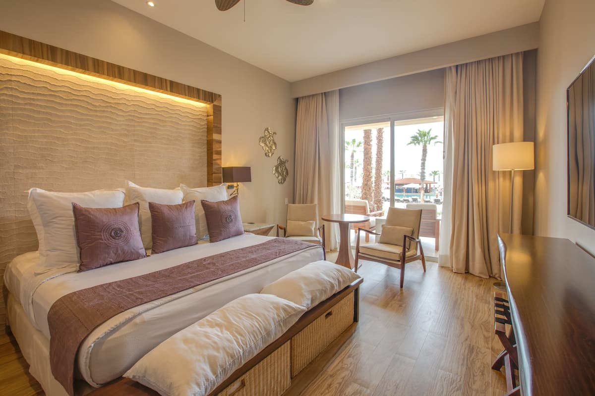 Une chambre d’hôtel avec un grand lit, une table de chevet, une chaise, une petite table et une vue sur l’extérieur.