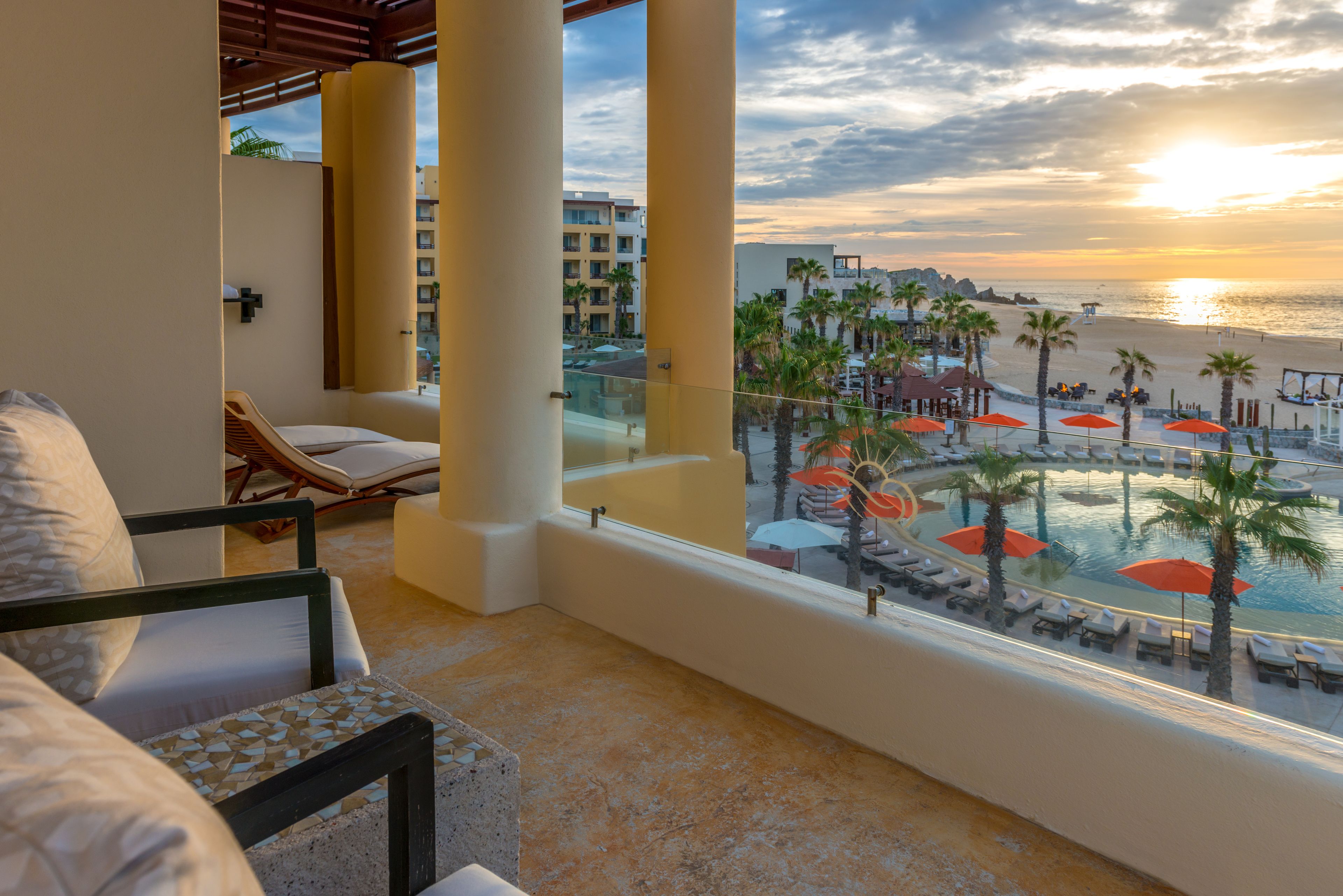 Varanda com vista para um resort à beira-mar, incluindo cadeiras de praia e guarda-sóis.