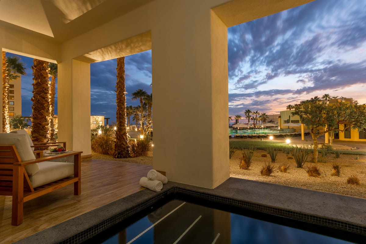 Un espace piscine doté d’une terrasse en bois, de chaises longues et offrant une vue sur le coucher de soleil au-dessus de la ligne d’horizon de la ville.
