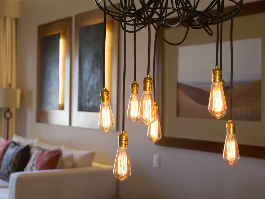 A living room with a sofa, a chandelier with multiple light bulbs, and artwork on the wall.