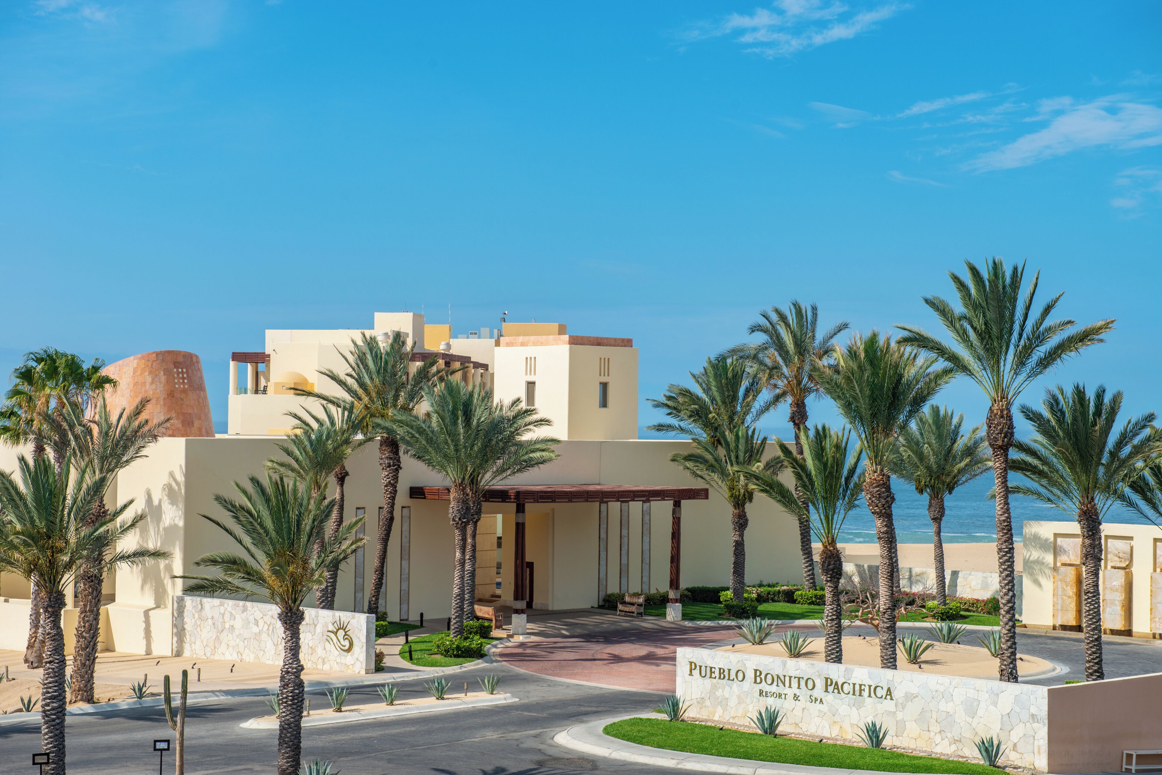 Ett semesterhotell med en skylt som visar texten ”Pueblo Bonito Pacifica Resort & Spa” och palmer i förgrunden.