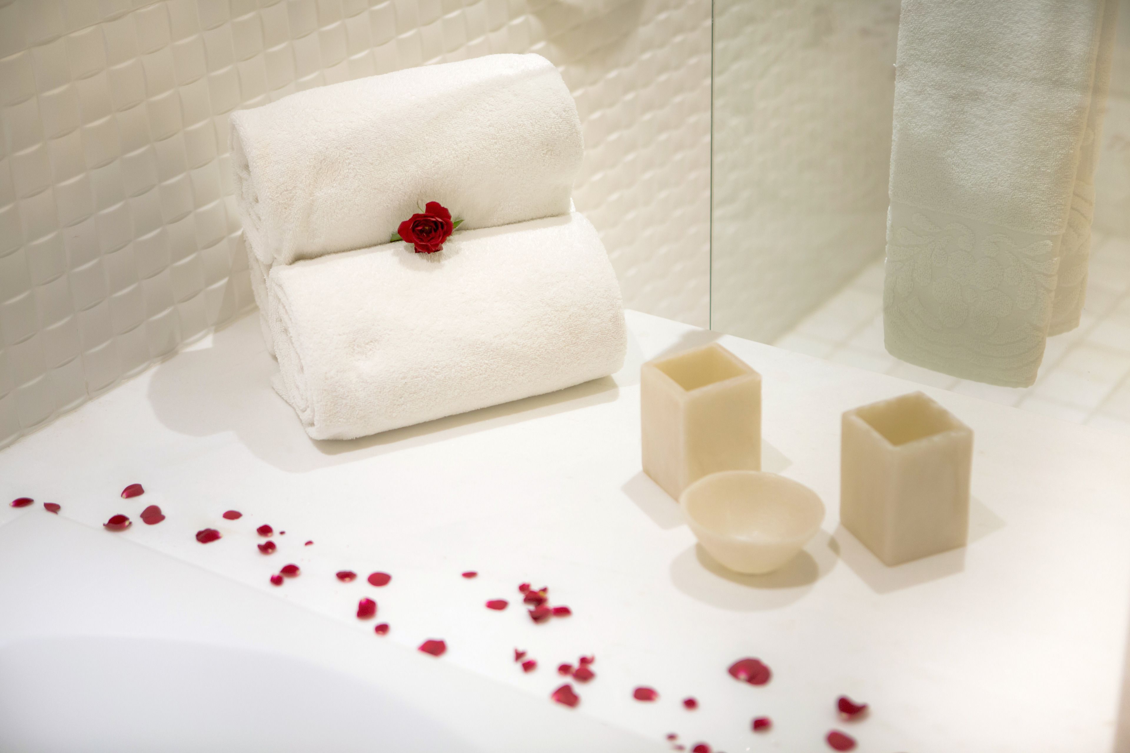 Une salle de bain bien rangée, avec une serviette blanche, une rose rouge et trois savons sur une surface blanche.