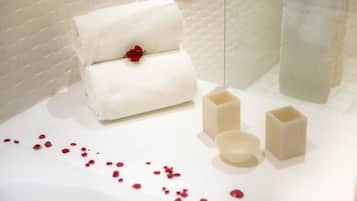 Um banheiro bem organizado com uma toalha branca, uma rosa vermelha e três barras de sabão sobre uma superfície branca.