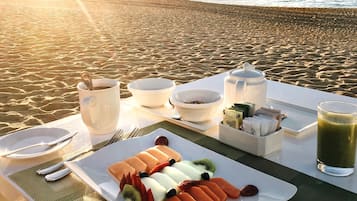 Un petit-déjeuner est préparé sur la plage, avec une table, des assiettes, des couverts et un verre de jus vert.