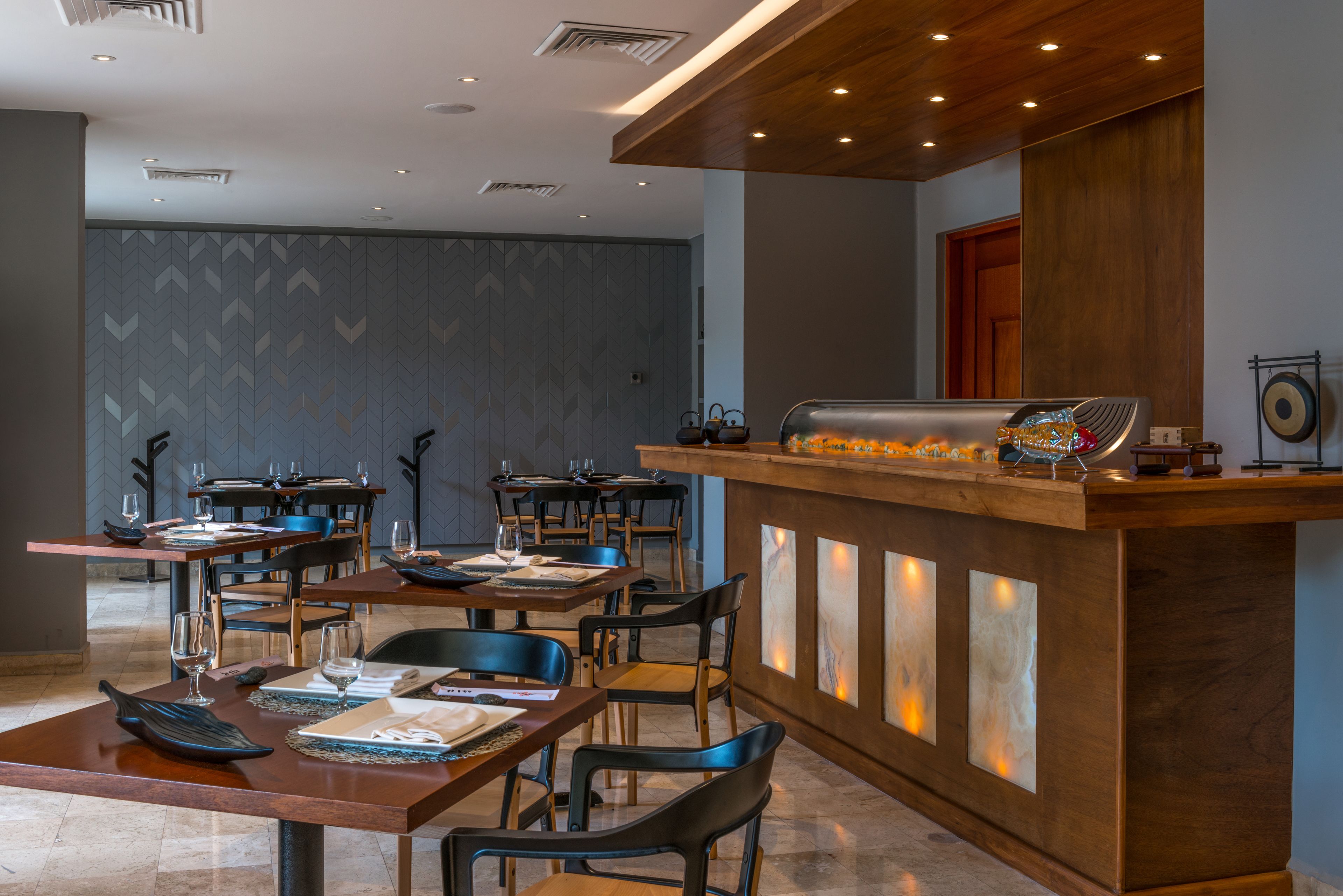 Un restaurante con mesas y sillas de madera, una barra con un mostrador decorativo y una pared con diseño.