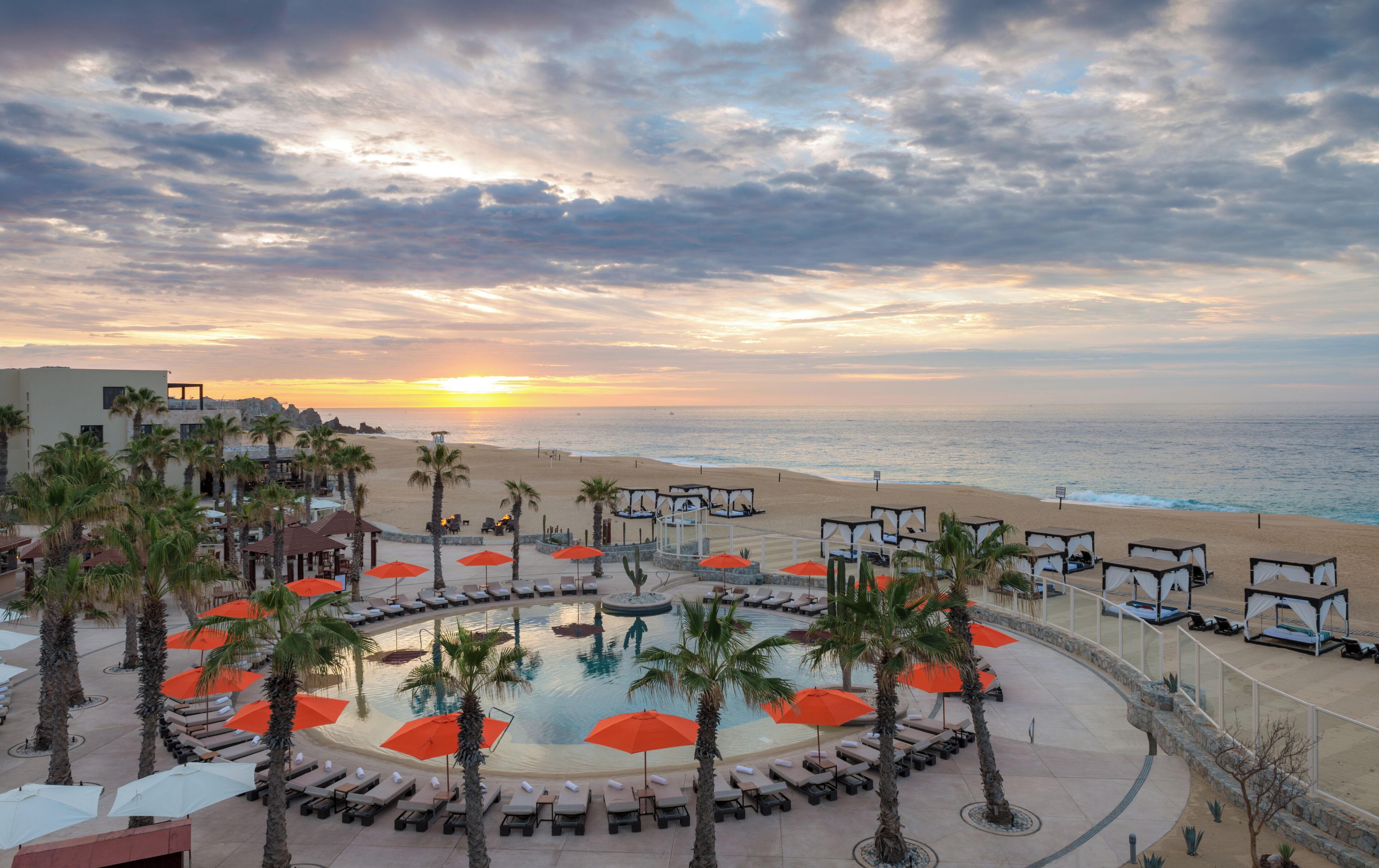 Un resort con piscina, tumbonas y sombrillas, con vistas a una playa y al océano.