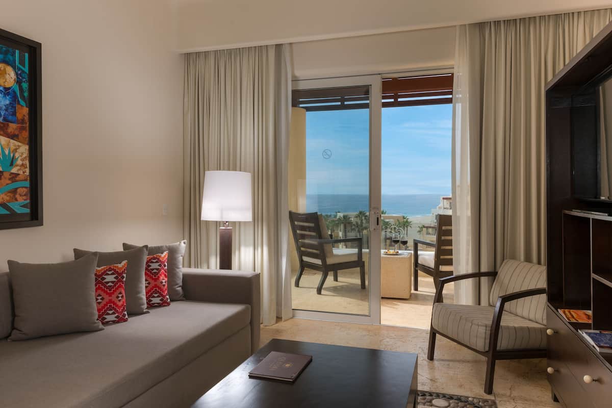 Une chambre d’hôtel équipée d’un canapé, d’une table basse, d’un fauteuil, d’une télévision et d’un balcon avec vue sur l’océan.