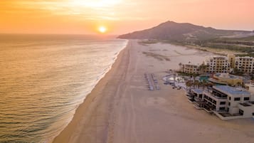 Um resort à beira-mar com uma extensa faixa de areia, área de piscina e montanhas ao fundo.