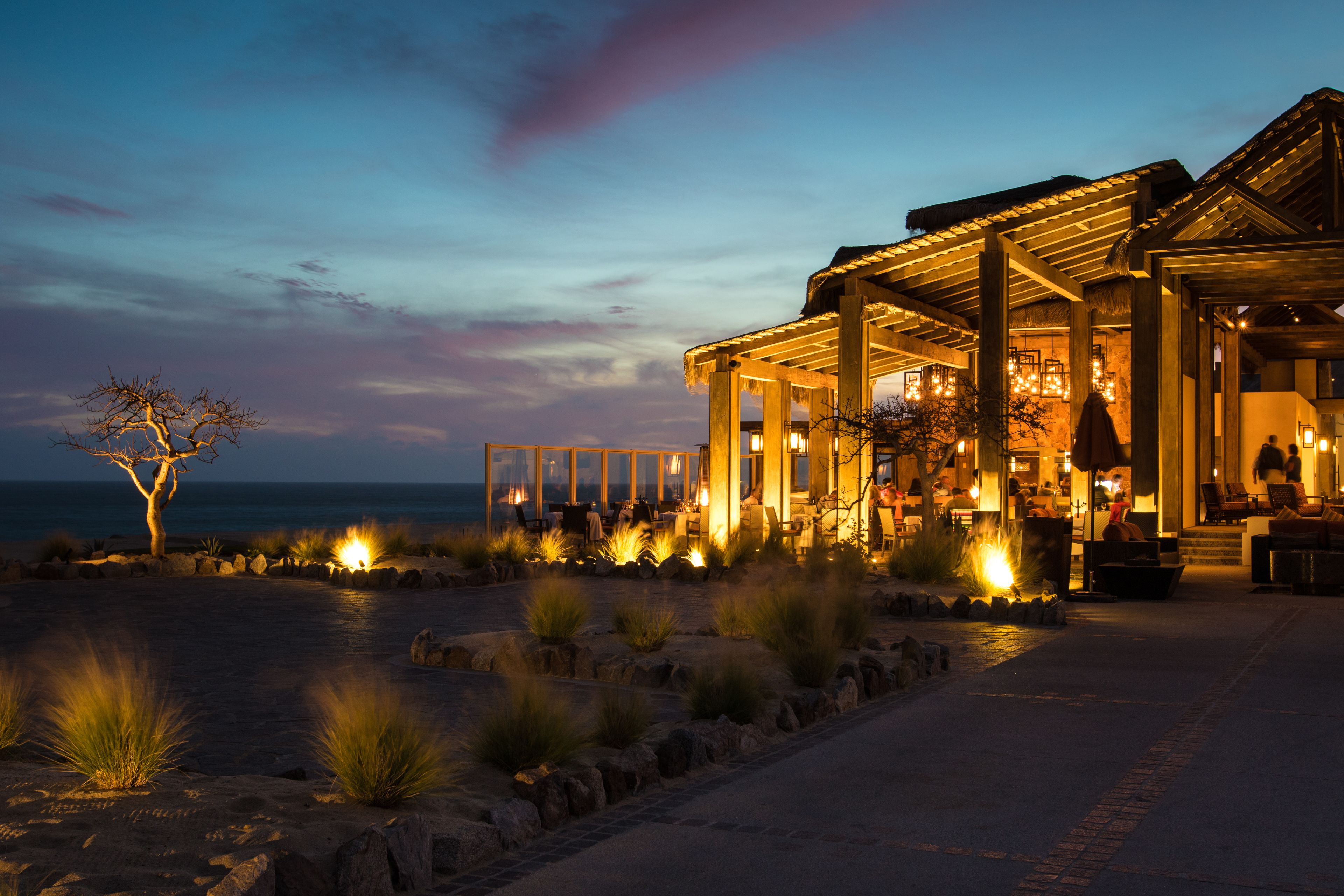 A beachfront hotel with an open patio, outdoor seating, and a view of the ocean.