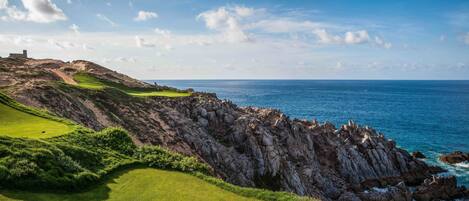 A coastal golf course with a rocky cliff and ocean view.