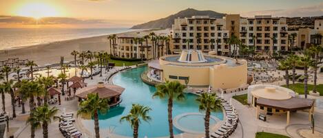 A resort with a central pool, multiple lounge areas, and a view of the beach and mountains.