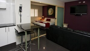 A compact hotel room with a kitchenette, a bed with red bedding, a TV mounted on the wall, and a small seating area. - Jesmond Executive Villas (Jesmond)