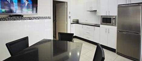A modern kitchen with white cabinets, a stainless steel refrigerator, a microwave, and a flat-screen TV mounted above the counter.