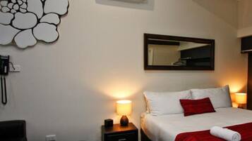 A hotel room with a bed, bedside lamps, a mirror, an air conditioning unit, and a wall decoration.