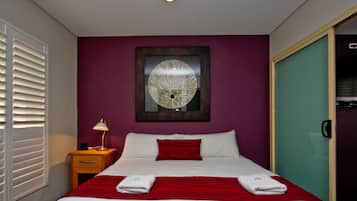 A hotel room with a bed, a nightstand, a lamp, a mirror, and a door.