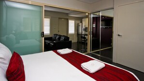 A hotel room with a bed, a red and white striped bedspread, two white towels, a black leather sofa, and a glass door leading to a bathroom. - Jesmond Executive Villas (Jesmond)