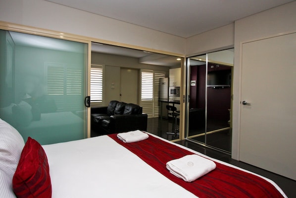 A hotel room with a bed, a red and white striped bedspread, two white towels, a black leather sofa, and a glass door leading to a bathroom. - Jesmond Executive Villas (Jesmond)