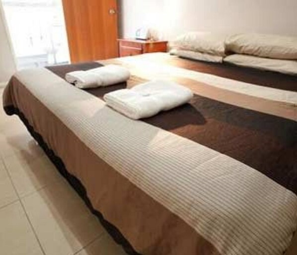 A hotel room with a large bed, a wooden nightstand, and a window with curtains. - Jesmond Executive Villas (Jesmond)