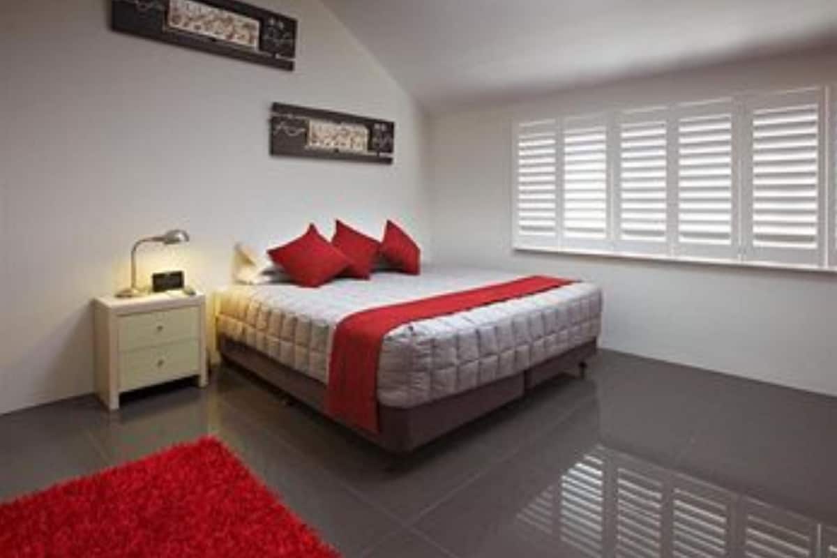 Une chambre à coucher avec un lit, une table de chevet, un tapis rouge et une fenêtre avec des stores.