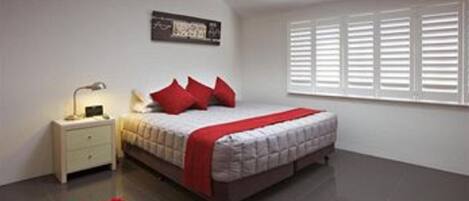 A bedroom with a bed, nightstand, red rug, and a window with blinds.