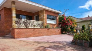 A two-story brick house with a front porch, a small garden with colorful flowers, and a clear blue sky. - Jesmond Executive Villas (Jesmond)