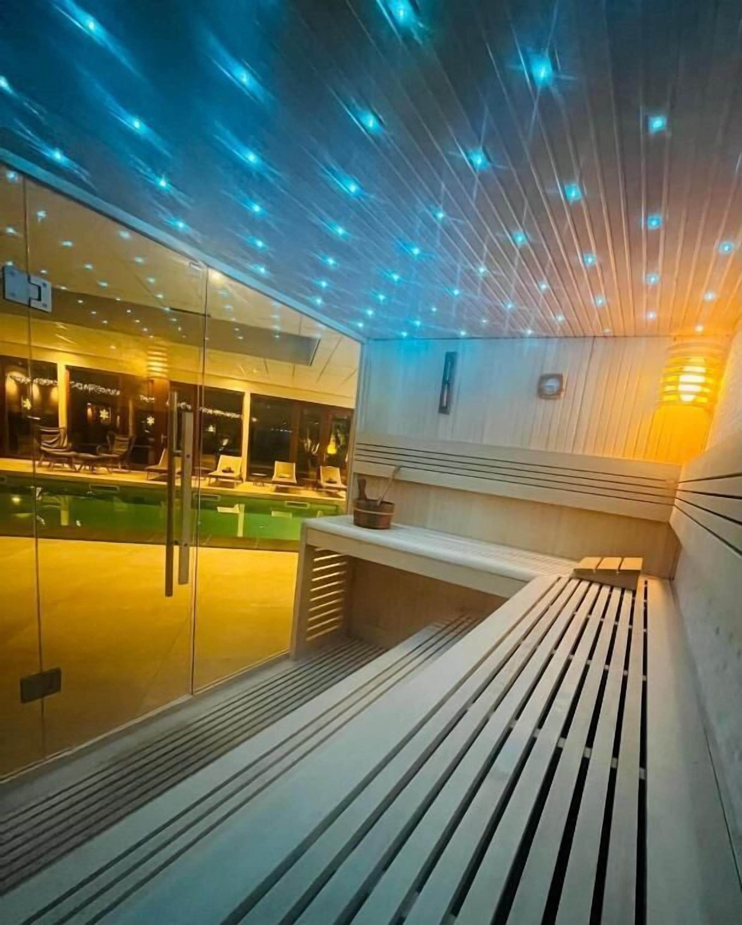 A modern indoor pool area with a bench, glass walls, and ceiling lights.