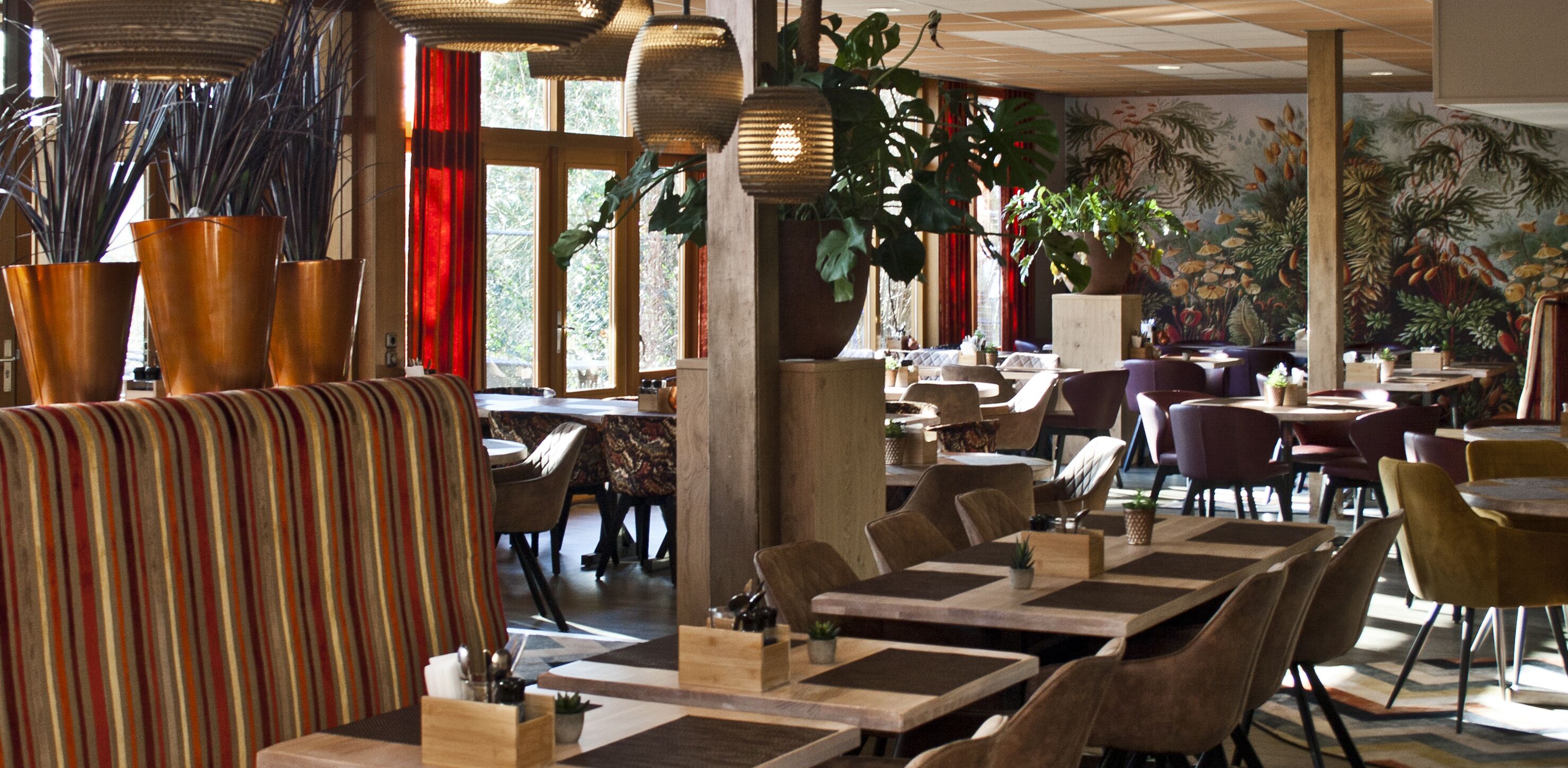 A restaurant with striped seating, wooden tables, and large potted plants.