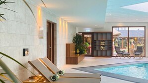 Un área de piscina interior moderna con sillones de descanso y vistas al exterior.