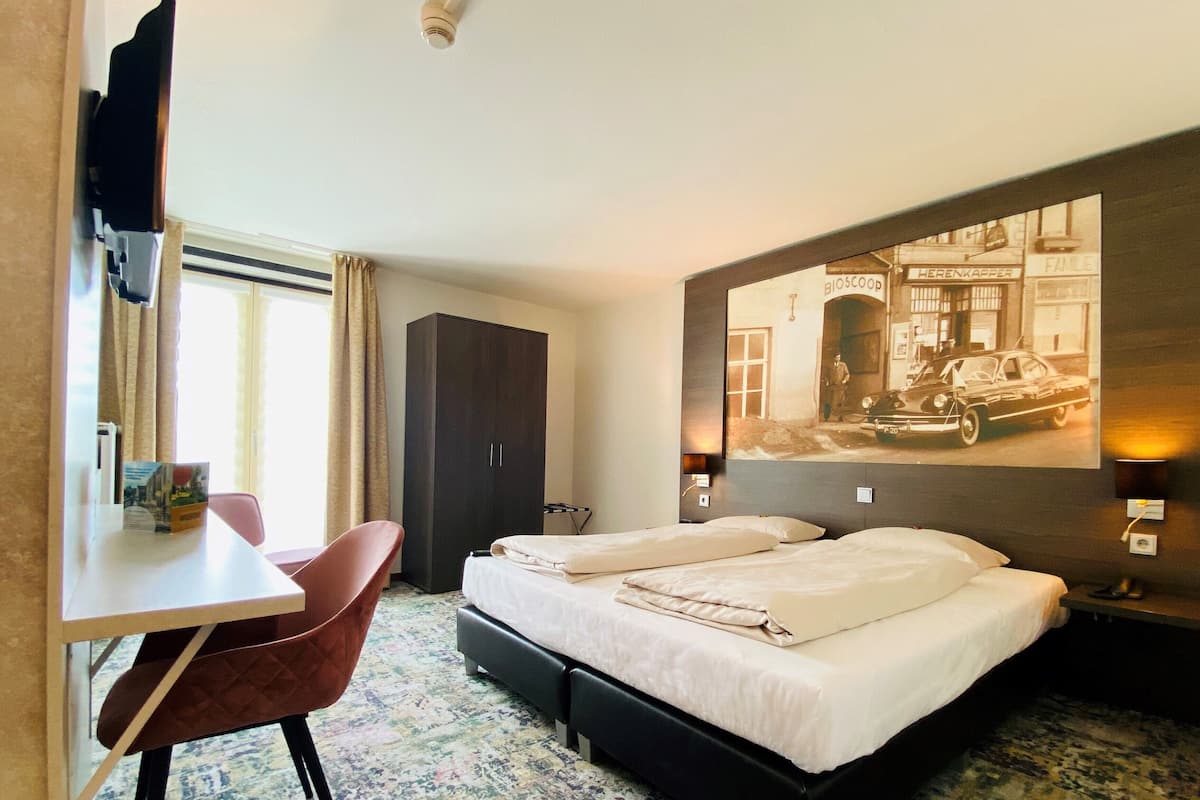 Een hotelkamer met een bed, een bureau, een stoel, een kledingkast en een aan de muur hangend schilderij.