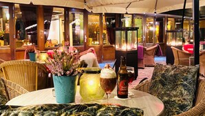 Un espacio al aire libre con mobiliario de mimbre, una mesa con una bebida y una vela, y un jarrón decorativo.