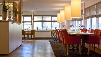 A modern dining area with a long table, multiple chairs, and pendant lighting.