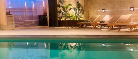 Piscina con sillones de descanso y zona de spa con sillón de masajes y plantas.