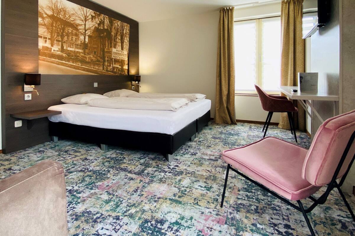 Een hotelkamer met een bed, een bureau, een stoel, een televisie en een groot schilderij aan de muur.