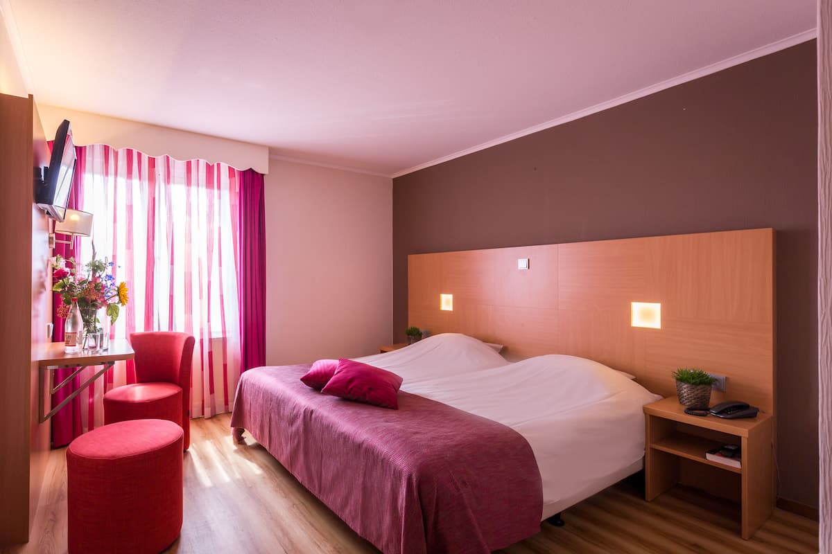 Een hotelkamer met een bed, een bureau, een stoel en een bijzettafeltje met een plant.
