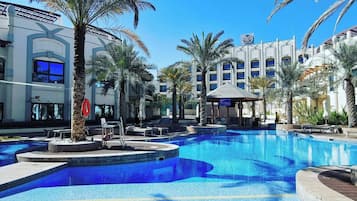 A swimming pool with lounge chairs and palm trees, surrounded by a building with multiple windows and a sign.