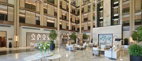 A spacious lobby with multiple seating areas, a high ceiling with a glass structure, and a modern design aesthetic.