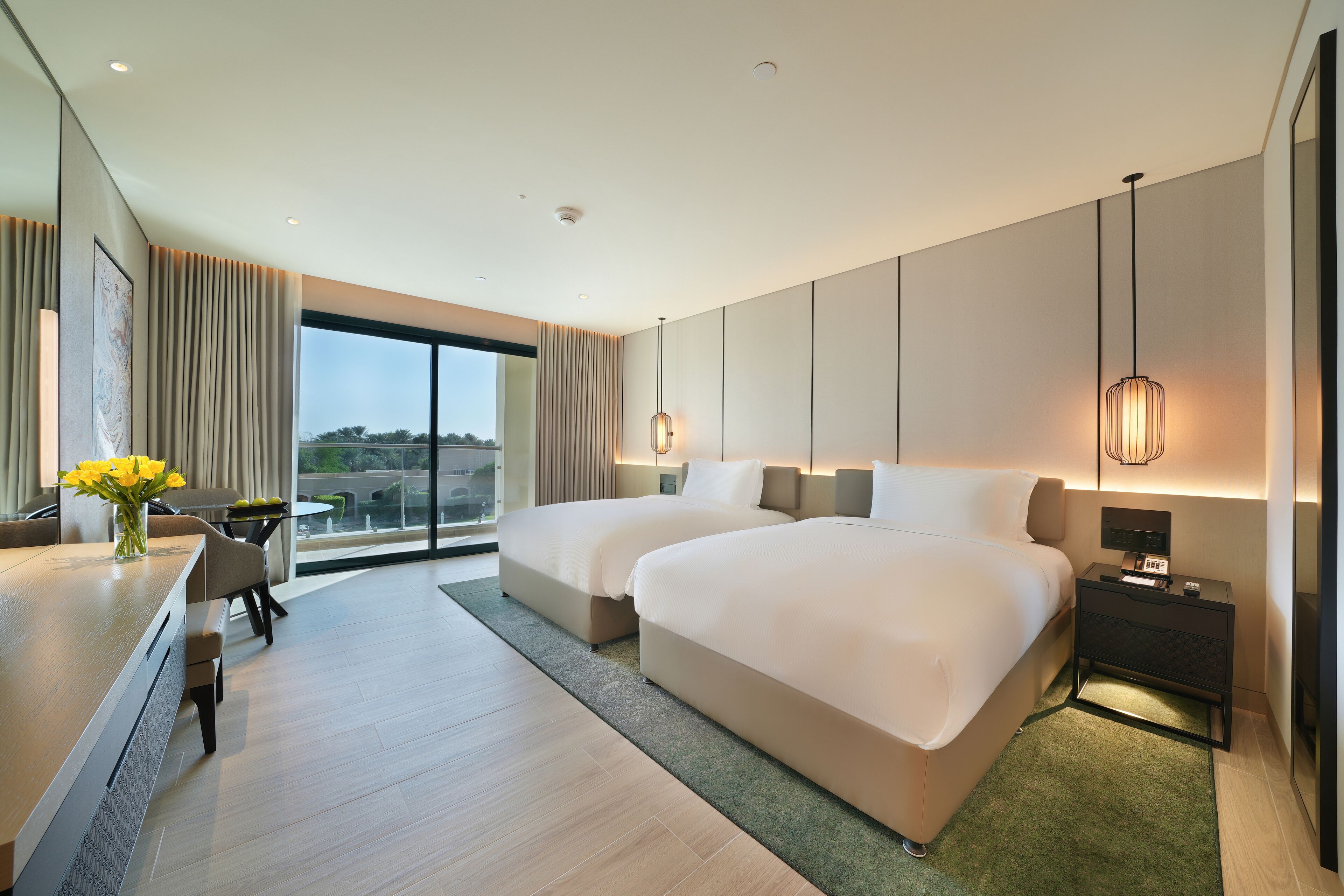 Quarto de hotel moderno com duas camas grandes, uma escrivaninha e vista para o exterior.