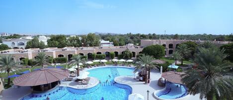 A large outdoor swimming pool with multiple sections, surrounded by palm trees and lounge areas.