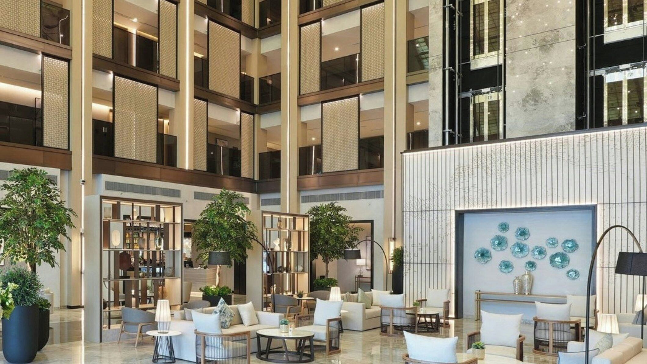 A spacious lobby with multiple seating areas, large windows, and a decorative wall with blue glass pieces.