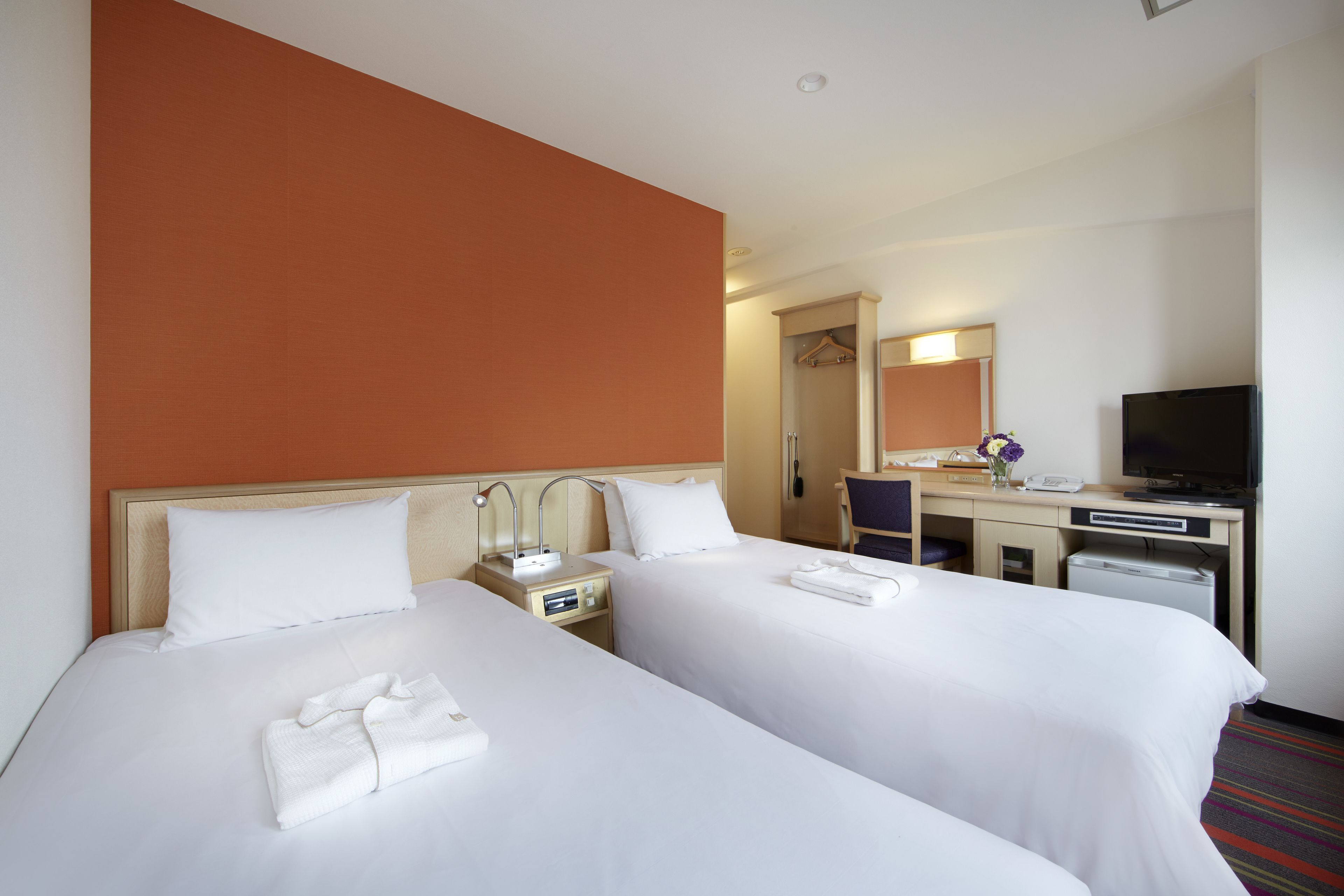 A hotel room with two beds, a desk with a computer, a television, and a mirror.