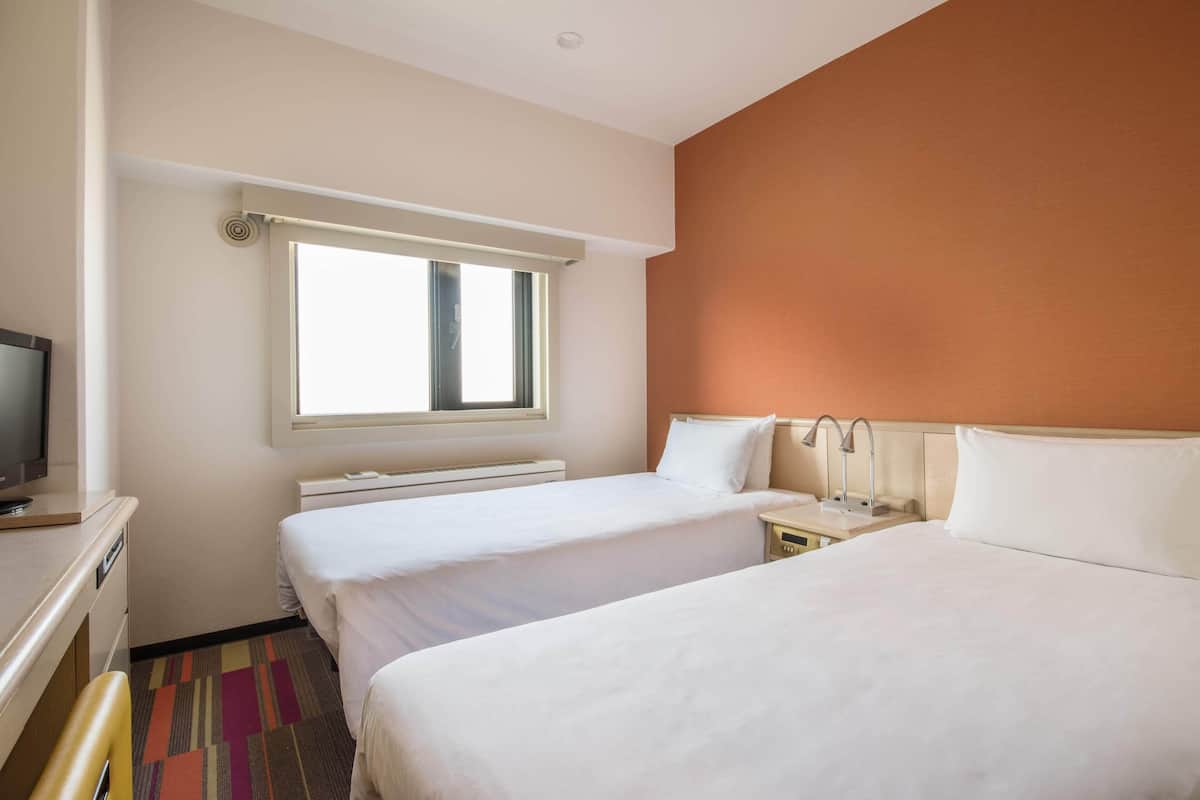 A hotel room with two beds, a TV, a window, and a bathroom with a mirror and sink.