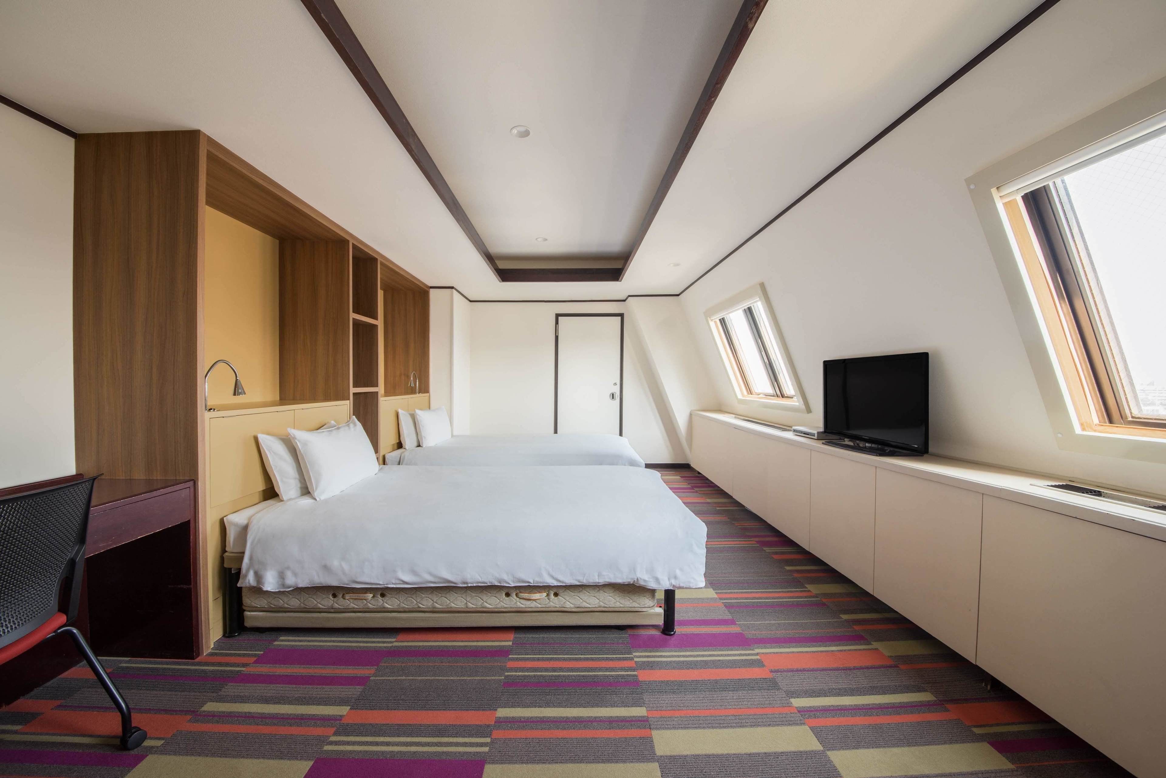 A hotel room with a bed, a desk, a TV, and a window.