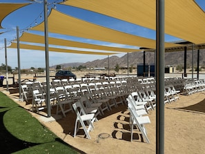 A covered outdoor seating area with white plastic chairs and tables, set against a desert backdrop with mountains. - Starlight Inn & Suites Motel 29 Palms Joshua Tree National Park (Twentynine Palms)