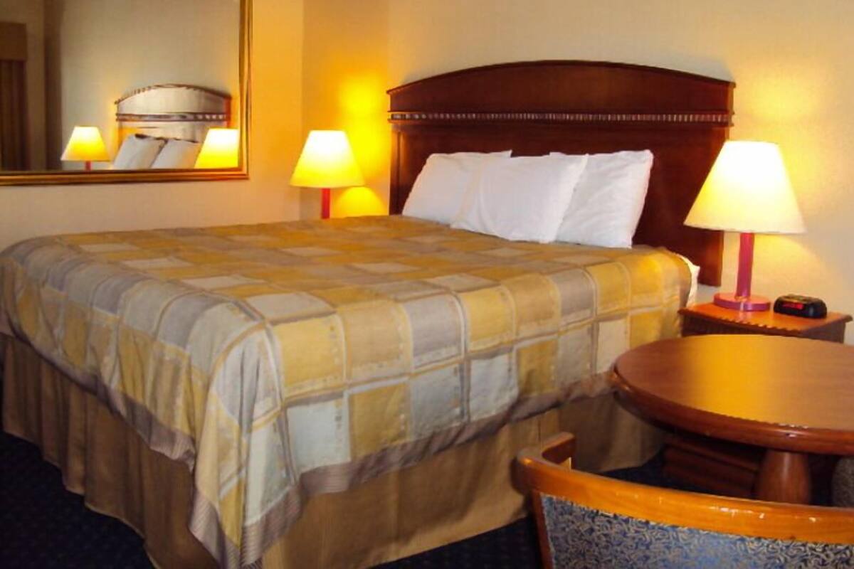 A hotel room with a bed, two bedside lamps, a round wooden table, and a chair.