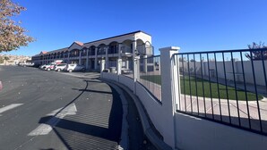 Un hôtel à la façade blanche, doté de nombreux balcons et d’un parking sécurisé par une grille.