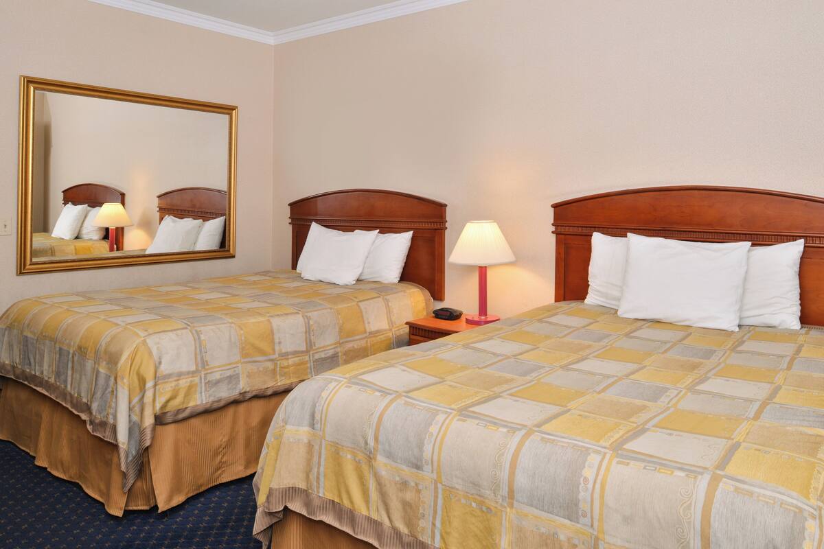 A hotel room with two beds, each with a wooden headboard, a large mirror, and bedside lamps.