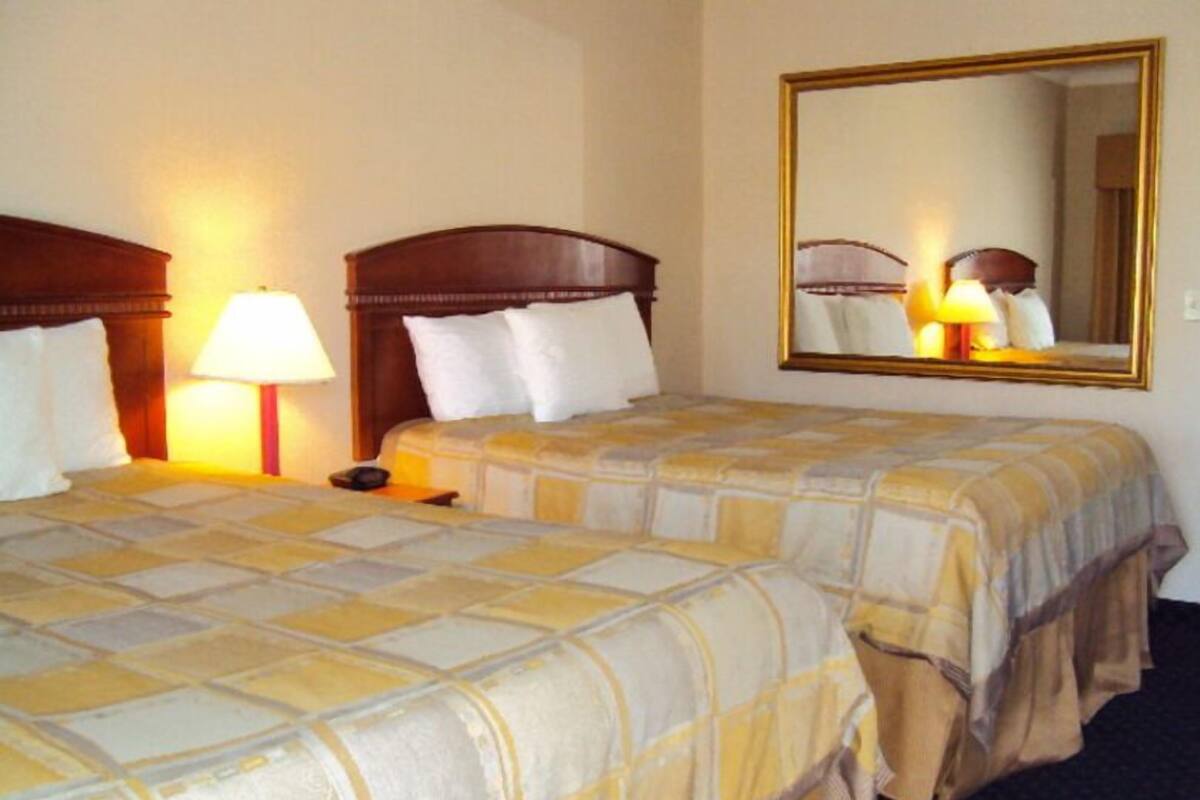 A hotel room with two beds, each with a headboard and a bedside lamp.
