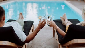 Two people sitting by a pool with drinks, lounge chairs, and a clear view of the pool. - Chalet View Lodge (Portola)